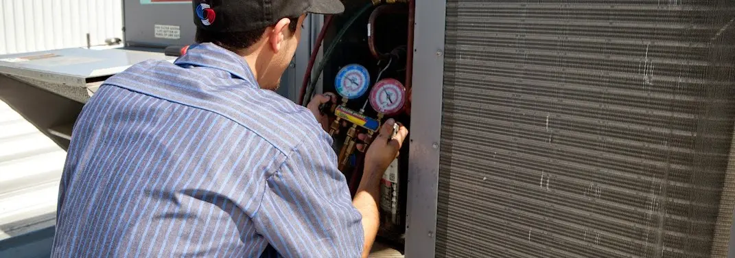 HVAC technician servicing a condenser unit in Oscoda